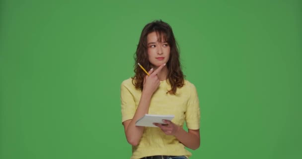 Happy pensive young modern girl make notes in notepad, planning, writing to do list, wishes, dreams on green background — Video Stock