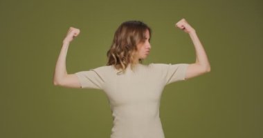 Kollarını kaldıran gururlu genç bir kadın kol kaslarını gösteriyor. Kas kasları, eğitimden sonra elde edilen başarılar.