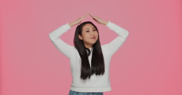 Hübsche asiatische Mädchen machen Dachhaus Geste über Kopf Stick Zunge auf rosa Hintergrund. Lebensversicherung, Sicherheitskonzept — Stockvideo