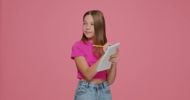 Увлеченная маленькая девочка, пишущая в тетрадке, размышляя над трудной задачей, придумывает классную идею почувствовать проницательность — стоковое видео