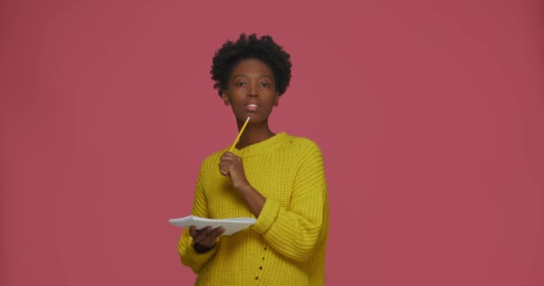 Usmívající se mladá africká americká dívka, která píše poznámky do notepadu, plánuje, přichází s nápady, cítí inspiraci — Stock video