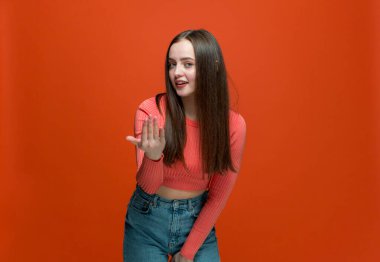 Buraya gel, beni takip et. Modern genç kız el ele arıyor, işaret ediyor, turuncu arka plana davet ediyor.