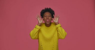 Oyuncu Afro-Amerikan genç kadın komik yüzler gösteriyor, jest yapıyor, dil ve ellerle yüzünü buruşturuyor, alay ediyor, eğleniyor. 