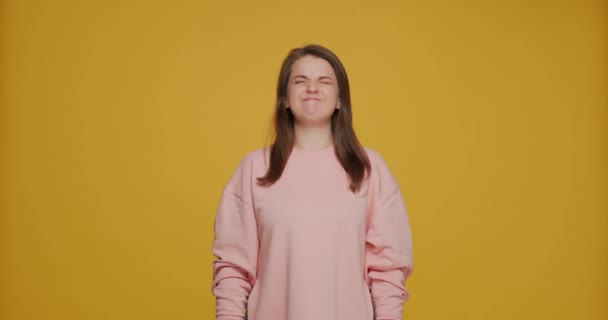 Funny young girl making faces, comical crazy grimacing, make audience laugh, fooling on yellow studio background — Vídeo de Stock