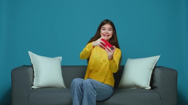 Carefree funny girl playing video game on mobile phone sitting at sofa, having fun with online entertainment and lose — Stock video