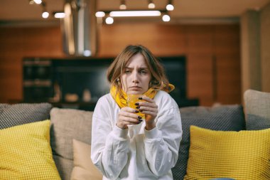 Sick young woman sitting on couch drink medicine, taking cough syrup on sofa at home. Flu influenza treatment