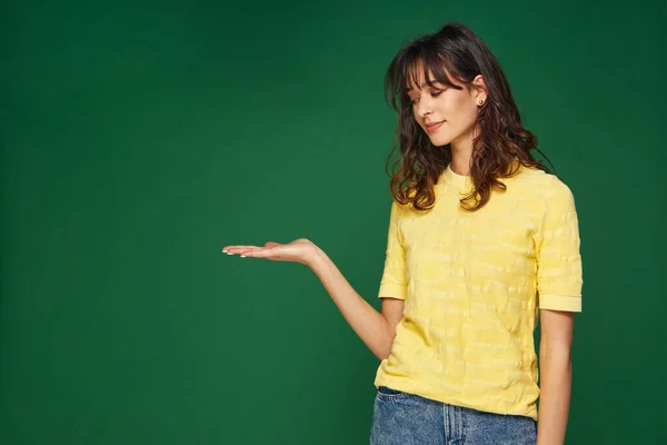 Pretty young girl holding blank copy space aside on palm, show advertising place with sale offer on green background — Stock Fotó