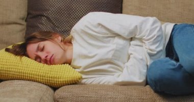 Unhealthy young woman suffering abdominal pain from menstruation, diarrhea, or indigestion lying on sofa at home