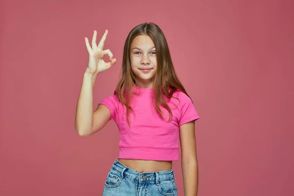 Ok sign. Cute child girl showing okay gesture accepting idea, giving positive feedback on pink studio background — Fotografia de Stock