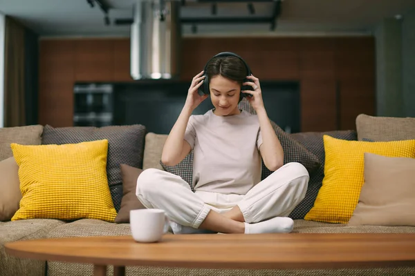 Modern young woman resting on sofa in wireless headphones enjoy weekend free time listen music, closed eyes — Stok fotoğraf