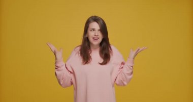 Dissatisfied outraged young girl spreading hands asking what, on yellow studio background. Misunderstanding, conflict