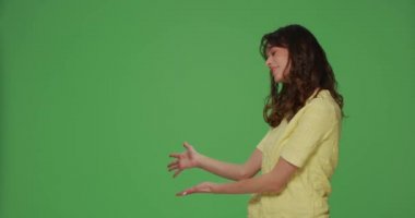Modern caucasian girl pointing at empty copy space with open palms, advertising product on green chromakey background