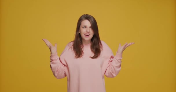 Dissatisfied outraged young girl spreading hands asking what, on yellow studio background. Misunderstanding, conflict — Stok video