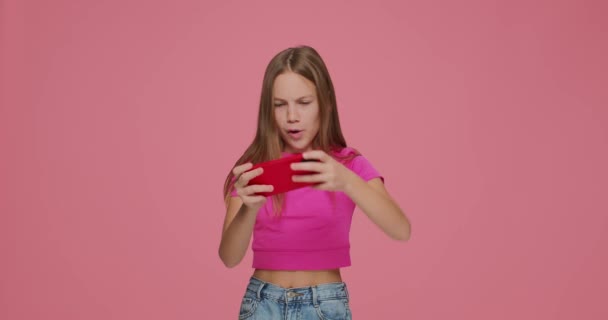 Gambling little girl gen Z gamer kid playing online virtual game on phone on pink studio background. Gadgets addiction — Stockvideo