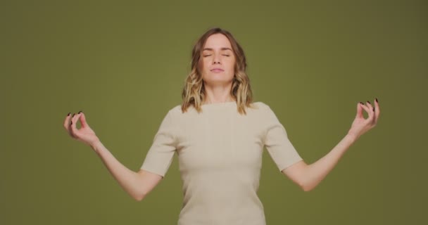 Young woman calming, breathing deep, meditating with mudra om gesture by hands, doing yogs exercise on green background — Stok video