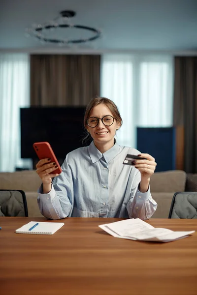 Smiling young woman make payment of taxes bills holding credit bank card using mobile phone application. E-commerce — Foto de Stock
