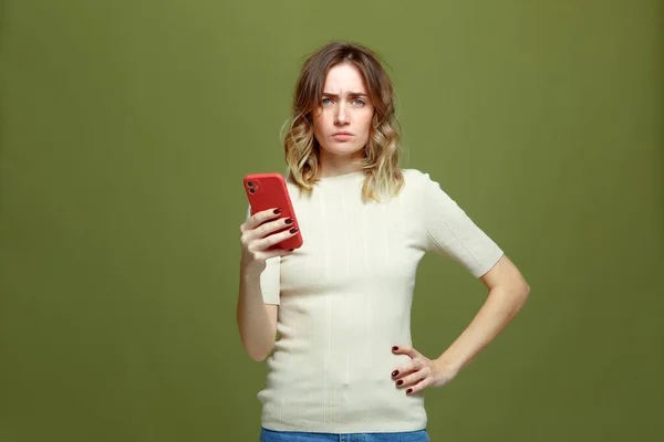 Sad young woman feel upset by bad news hold phone, suffer from bullying in social media on green studio background — Stockfoto