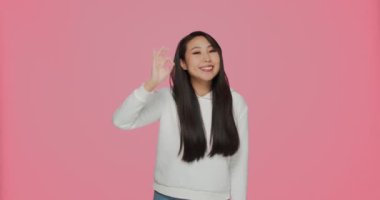 Happy asian young girl showing ok gesture, satisfied customer making okay sign recommend service on pink background
