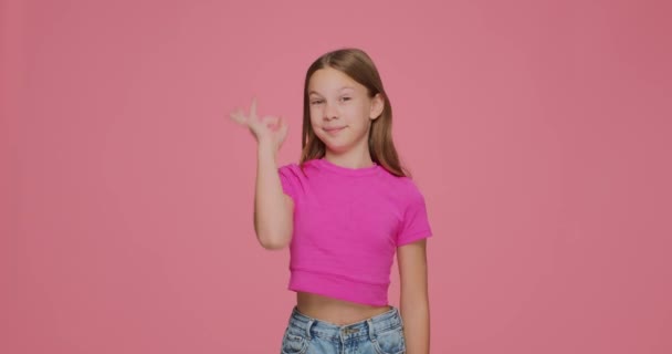 Забавна дівчинка, яка показує нормальний жест, робить окуляри пальцями, розважається, обманює рожевий фон. Позитивний відгук — стокове відео