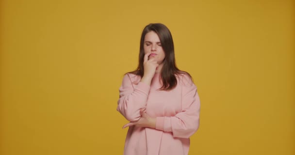 Pensive puzzled young girl solve cognitive task, make decision or choice on orange studio background with copy space — 비디오