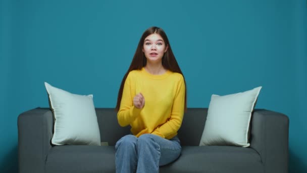 Pretty modern young girl making silence gesture, shushing, asking to keep quiet, sitting on couch. Unique sale offer — Wideo stockowe