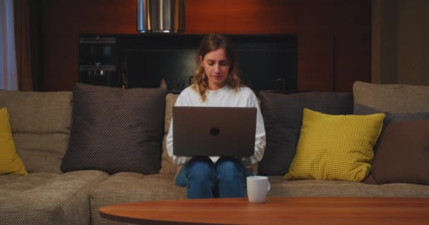 Креативна молода жінка фрілансер з ноутбуком працює в Інтернеті віддалено вдома, сидячи на дивані у вітальні. Віддалена робота — стокове відео