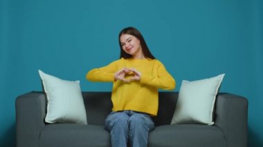 Dost canlısı genç kız blogcu, mavi arka planda, koltukta otururken aşk jesti gösteriyor. Sadaka ve bağış konsepti