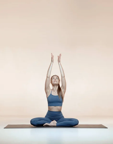 Jeune fille yogi sportive assise dans la pose de lotus sur tapis levant la main pendant le cours de yoga. Femmes bien-être, mode de vie sain — Photo