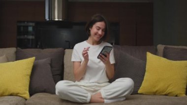 Bankacılık ya da bahis uygulaması kullanan şanslı genç kız para kazanıyor. Yağmur yağıyor. Evdeki koltukta oturuyor. Büyük ikramiye, finansal başarı.