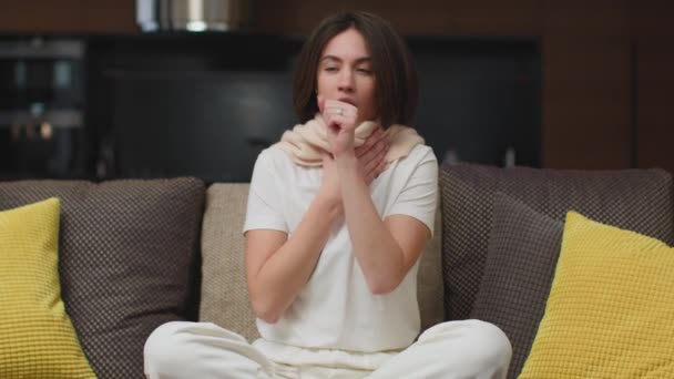 Нездоровая молодая девушка кашляет, страдает от гриппа или лихорадки, сидя на диване в гостиной дома на больничном — стоковое видео