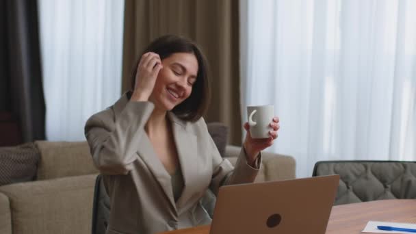 Радісна молода бізнес-леді сидить на ноутбуці з кавою, танцює під час перерви, розважається, задоволена успішною угодою — стокове відео