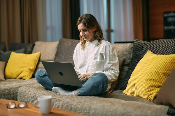 Dizüstü bilgisayarda çalışıp evdeki oturma odasında oturan mutlu genç yaratıcı kız. Uzak çevrimiçi görev — Stok fotoğraf