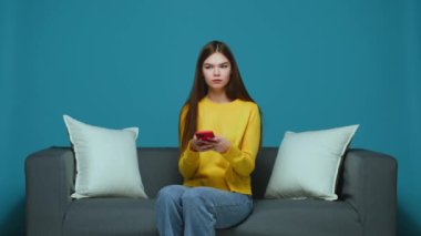 Telefonla rahatsız edilmiş genç bir kız, sosyal medyada hoş olmayan mesajlar alıyor, kanepede oturuyor, internette kavga ediyor.