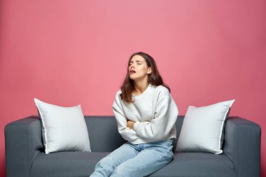 Sağlıksız kız karnına dokunuyor, karın ağrısı çekiyor, kanepede oturuyor. Mide bulantısı, mide ağrısı, acı dolu dönemler.