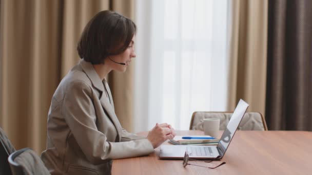 Przyjazna kobieta operator infolinii w słuchawkach trzymać rozmowy wideo, rozmawiać z klientem online na laptopie. Obsługa klienta — Wideo stockowe