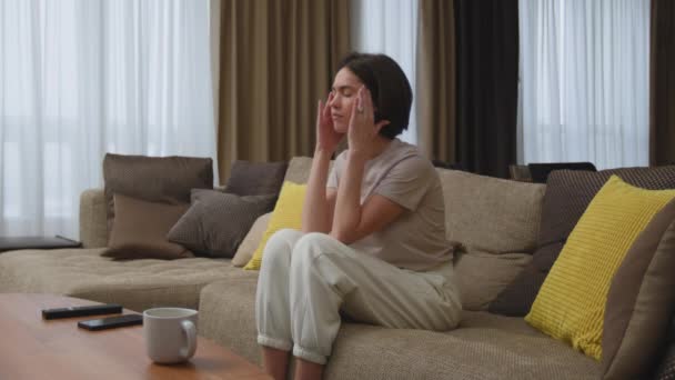 Cansado jovem mulher massageando templos, sofrer de dor de cabeça, enxaqueca, sentando-se estressado, sentado no sofá em casa — Vídeo de Stock