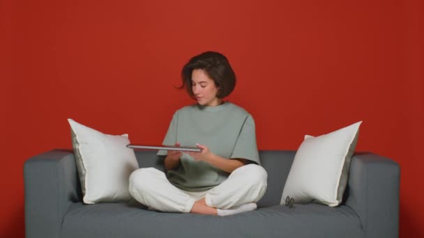 Freelance giorno lavorativo. Una ragazza sul divano usa un portatile per lavorare a distanza durante una pandemia. Sfondo rosso. — Video Stock