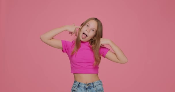 Anak perempuan hooligan keras kepala menempel jari-jari steker di telinga tidak mendengarkan, menolak mendengar, mengeluh, bermain-main pada latar belakang studio merah muda — Stok Video
