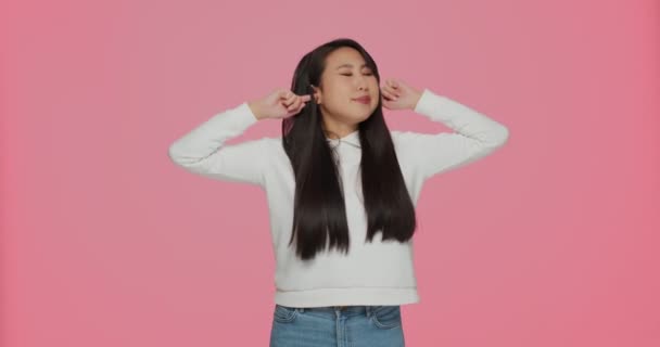 Young asian girl shout plugging ears with fingers unable to hear loud music noisy sound, nasty noise on pink background — Stock Video