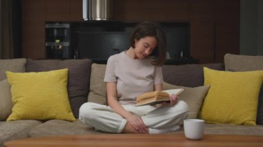 Güzel genç kız öğrenci, en çok satan roman okuyor, hafta sonunun tadını çıkarıyor, evdeki rahat kanepede oturuyor.