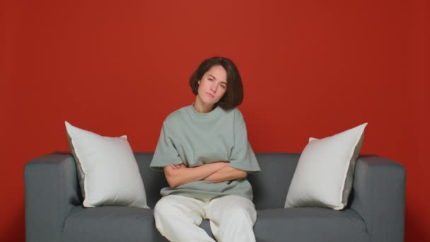 Eine enttäuschte und unzufriedene Ehefrau. In strenger Pose auf dem Sofa sitzend. Vereinzelt auf rotem Hintergrund. — Stockvideo
