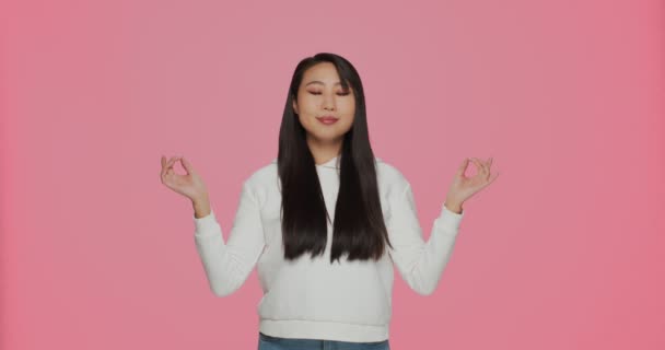 Ruhige asiatische Mädchen meditieren, atmen, Yoga praktizieren, macht Mudra-Geste auf rosa Hintergrund. Gesunder Lebensstil, Stressabbau — Stockvideo