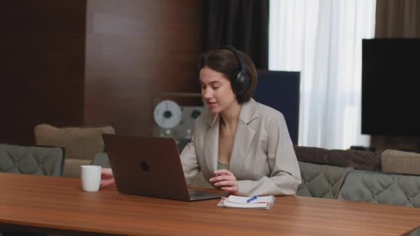 Funcionária no fone de ouvido sente-se na mesa trabalhando no laptop, faça uma videoconferência com colega ou cliente. Trabalho remoto — Vídeo de Stock