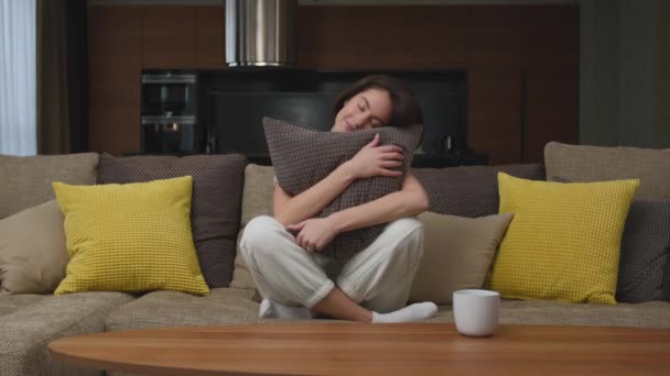 Calma giovane donna sorridente abbracci cuscino seduto su accogliente divano in soggiorno a casa, riposo, godersi il fine settimana — Video Stock