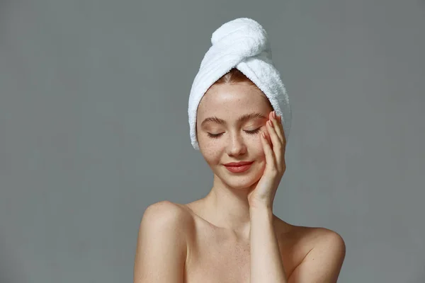 Όμορφη νεαρή κοπέλα με πετσέτα στο κεφάλι, γυμνοί ώμοι, αγγίζει μαλακό υγιές δέρμα. Διαφήμιση καλλυντικών καλλωπισμού ομορφιάς — Φωτογραφία Αρχείου