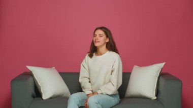 Gülümseyen genç kız göz kırpıyor, başını sallıyor evet, flört ediyor, ima ediyor, kanepeye oturuyor iyimserliğini ifade ediyor, olumlu duygularını ifade ediyor.