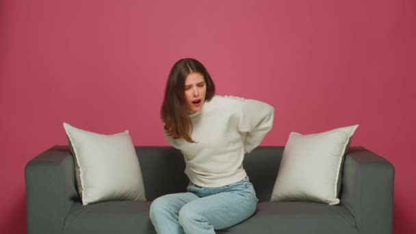 Rugpijn. Jong meisje lijden rugpijn, geknepen zenuw, raakt onderrug, zitten op de bank in ongemakkelijke pose — Stockvideo