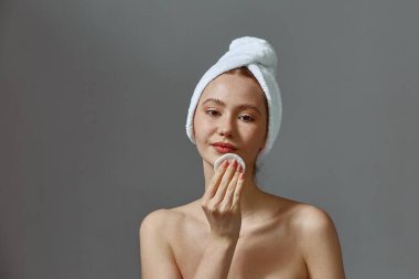 Çıplak omuzlu, yüzünü losyon ya da tonikle temizleyen genç bir kız. Pamuk pedi kullanıyor. Cilt bakımı, kozmetoloji konsepti