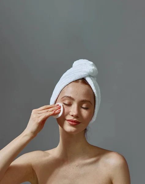Menina bonita com toalha na cabeça segurar algodão pad limpeza rosto pele remover maquiagem, desfrutar de rotina de beleza de cuidados com a pele — Fotografia de Stock