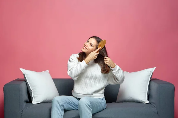 Piękna dziewczyna szczotka zdrowe błyszczące włosy przez szczotkę do włosów, preening, siedzi na kanapie. reklama kosmetyków do pielęgnacji włosów — Zdjęcie stockowe
